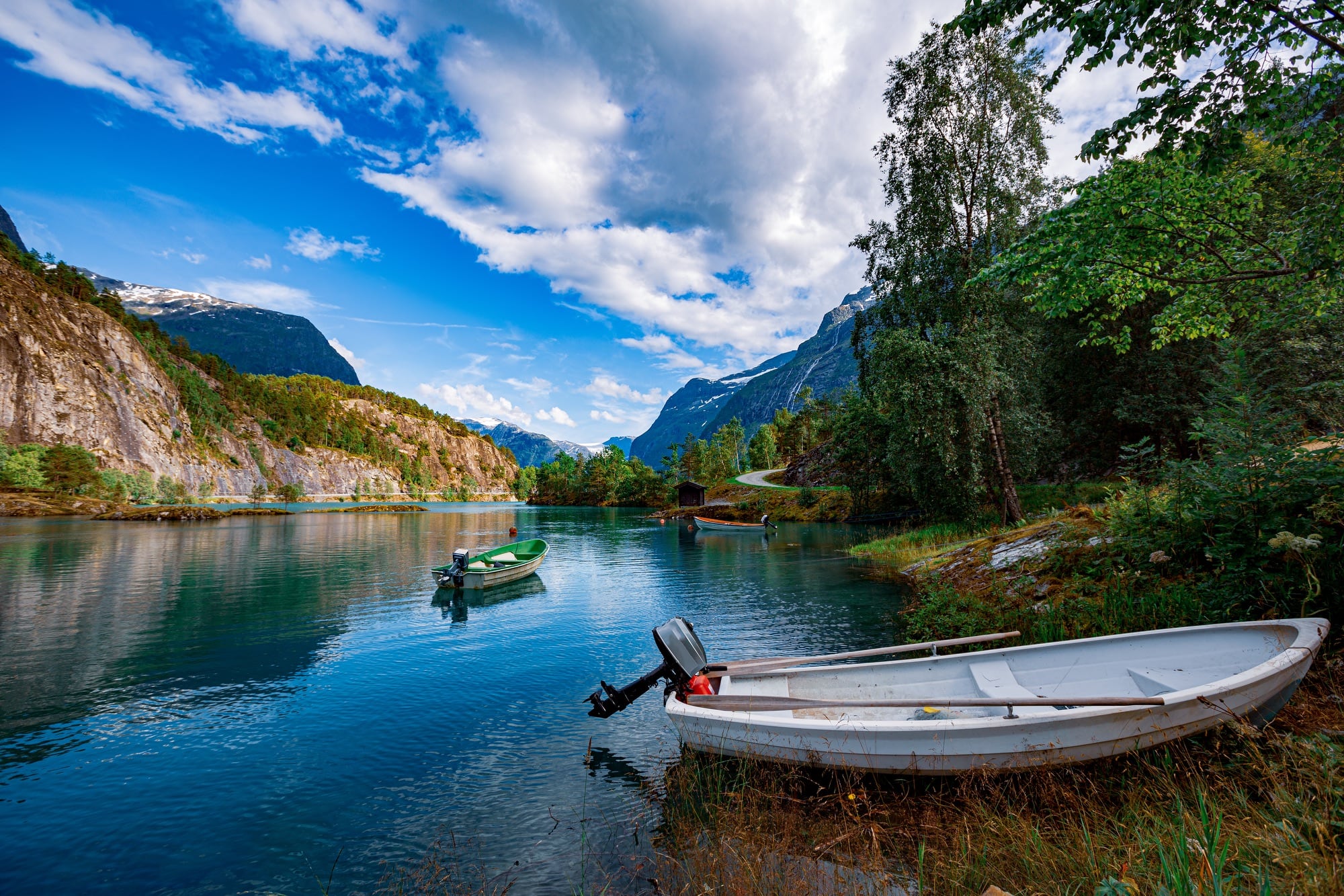 A small wooden boat with an outboard engine rests in the shallows of a lake in Norway.