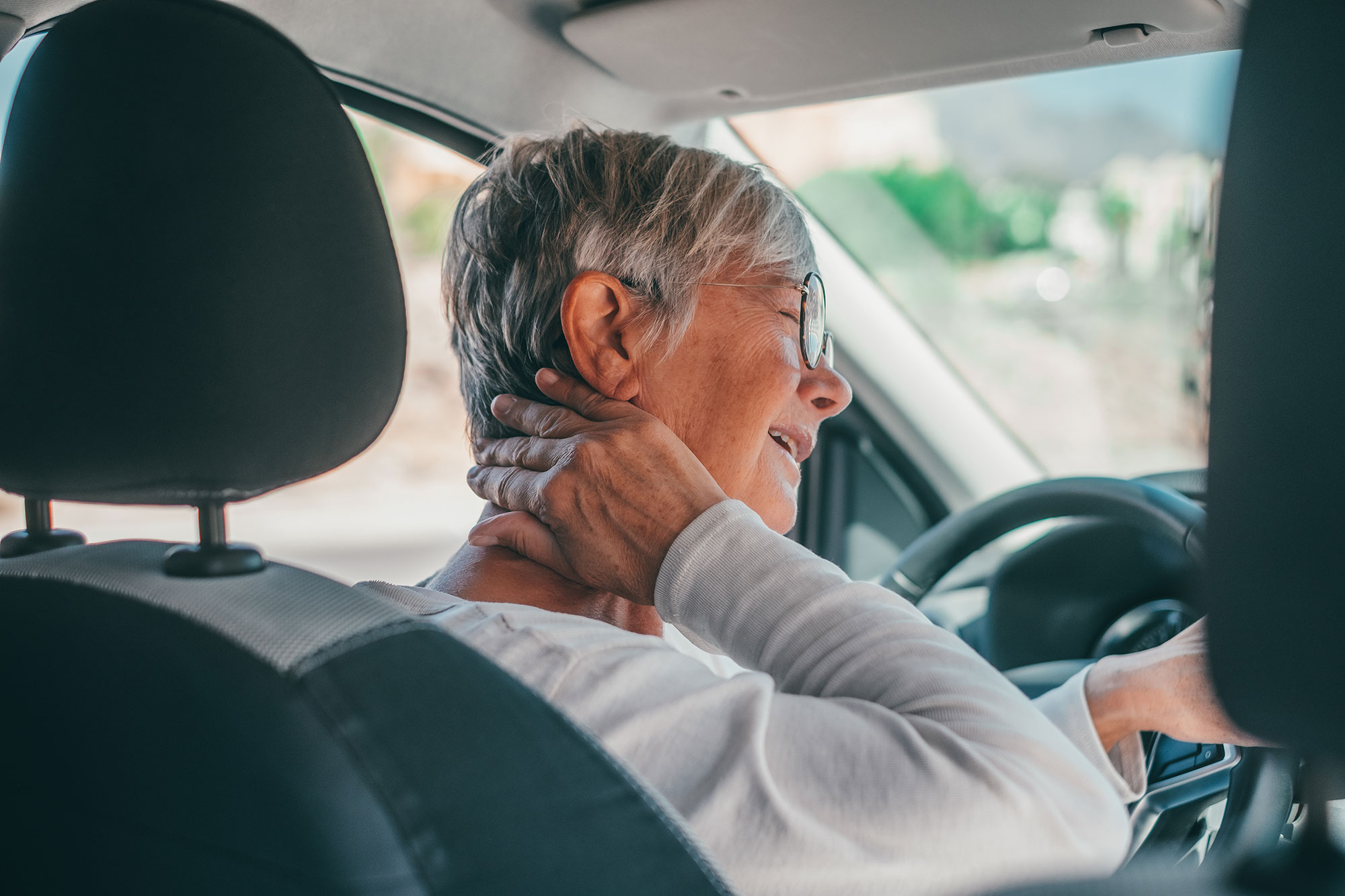 A woman in her car wincing and holding her hand to her neck, symbolizing pain caused by a motor vehicle accident.